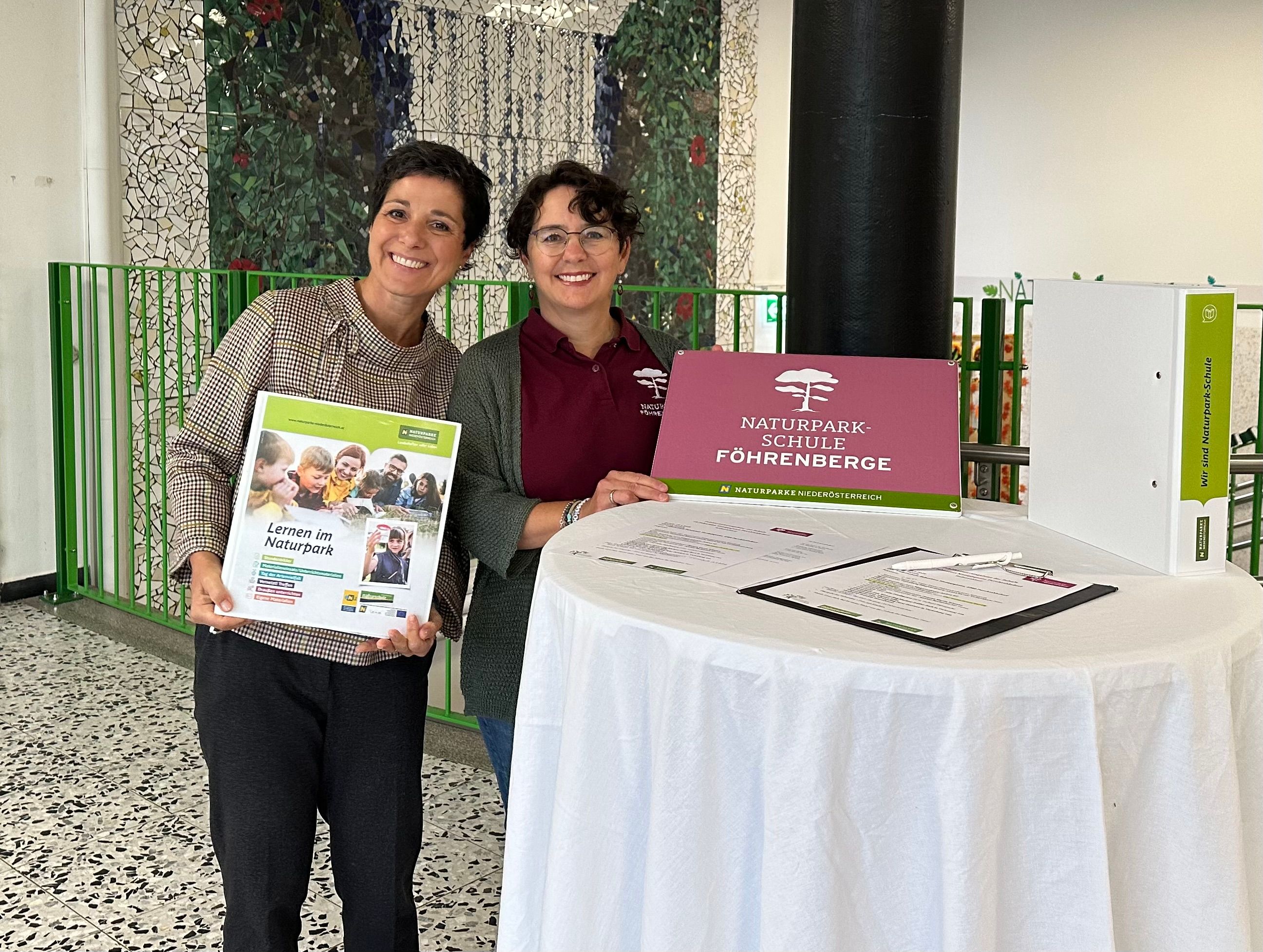 Elke Weisz-Emesz (Landschaftspflegeverein-Bildungsreferentin für den Naturpark Föhrenberge) und Jasmine Bachmann (Geschäftsführerin Verein Naturparke NÖ)  präsentieren die Urkunde.