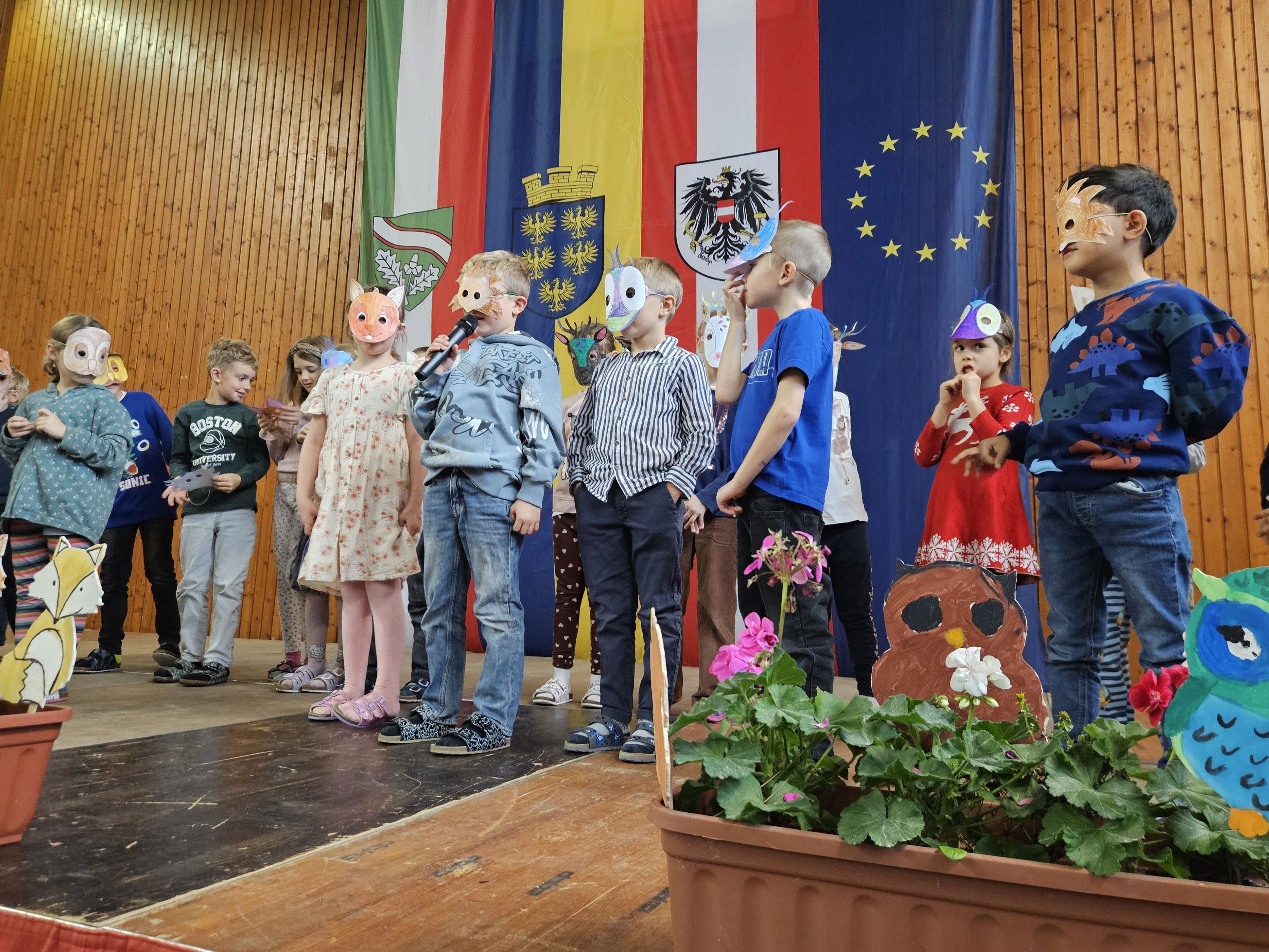 Kinder mit Tiermasken tragen auf der Bühne das Gedicht "Tiere im Wald" vor.