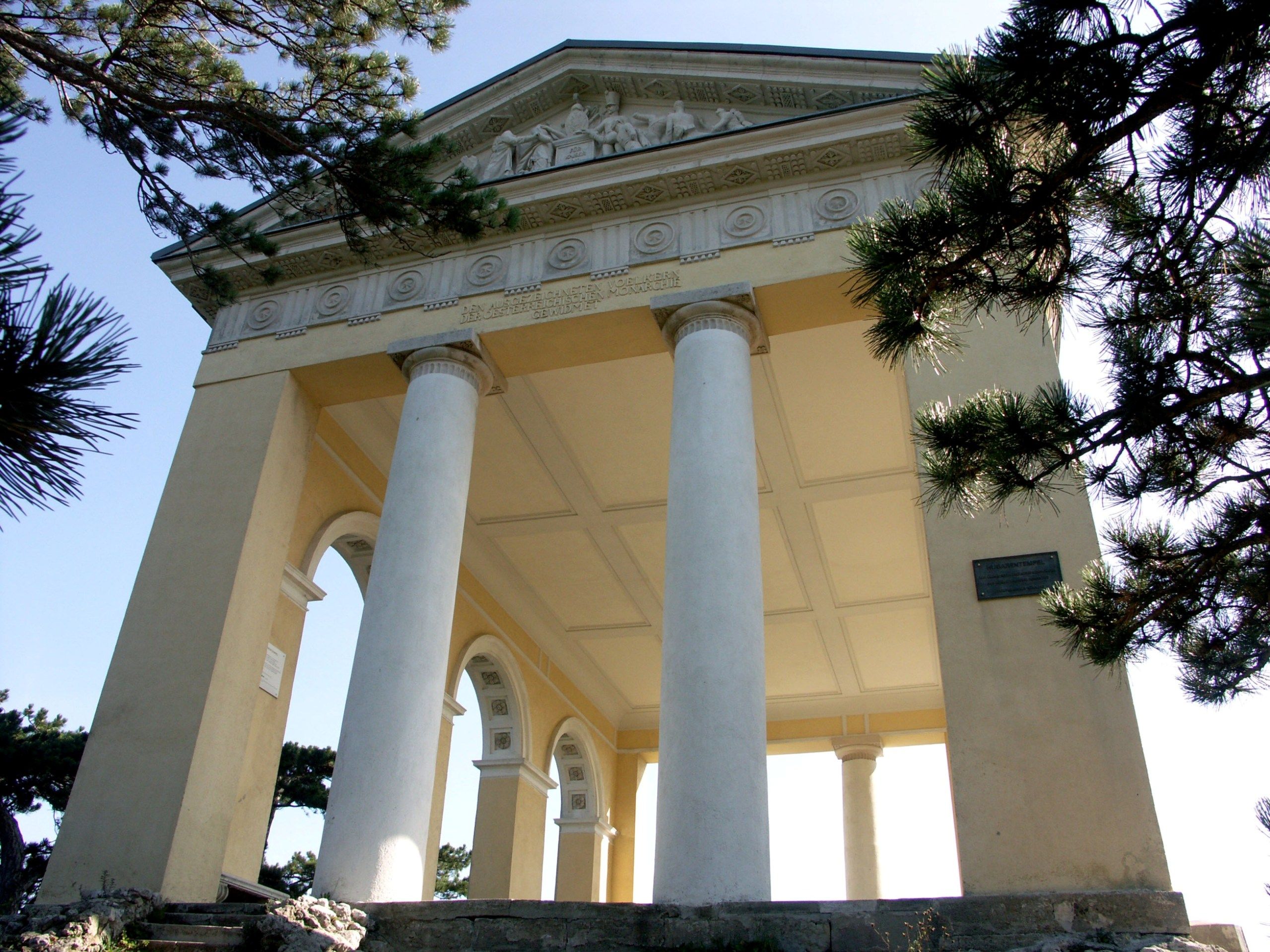 Der Husarentempel mit Säulen und Reliefs, umgeben von Bäumen.