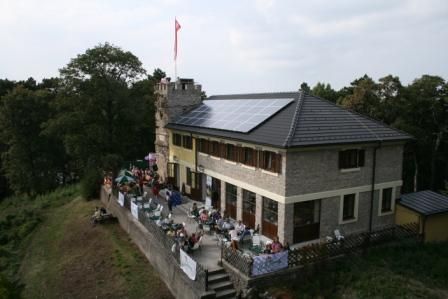 Höllensteinhaus mit Terrasse und Solarpanelen auf dem Dach, umgeben von Bäumen.
