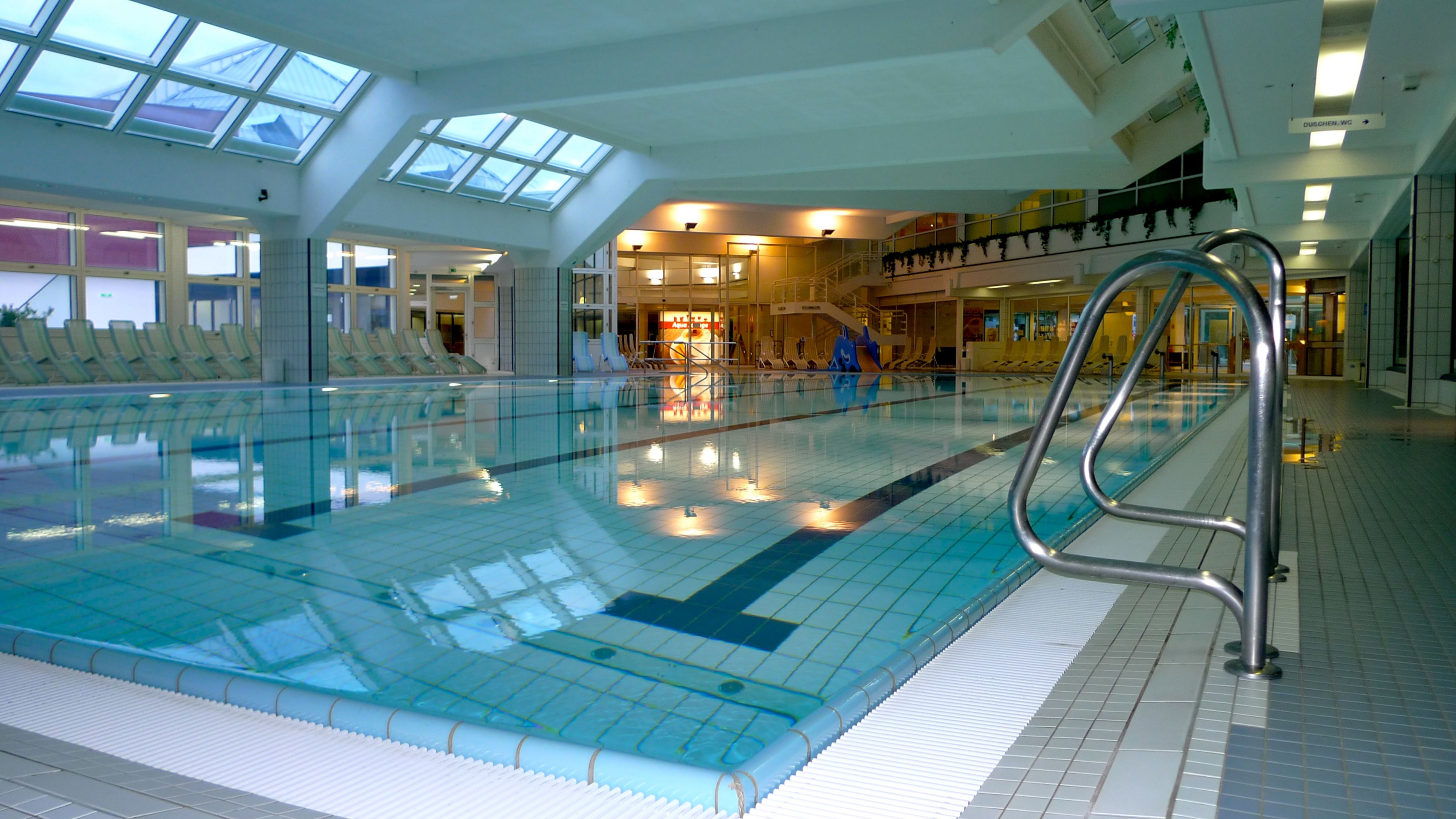 Innenansicht eines modernen Hallenbads mit Schwimmbecken und Liegestühlen.