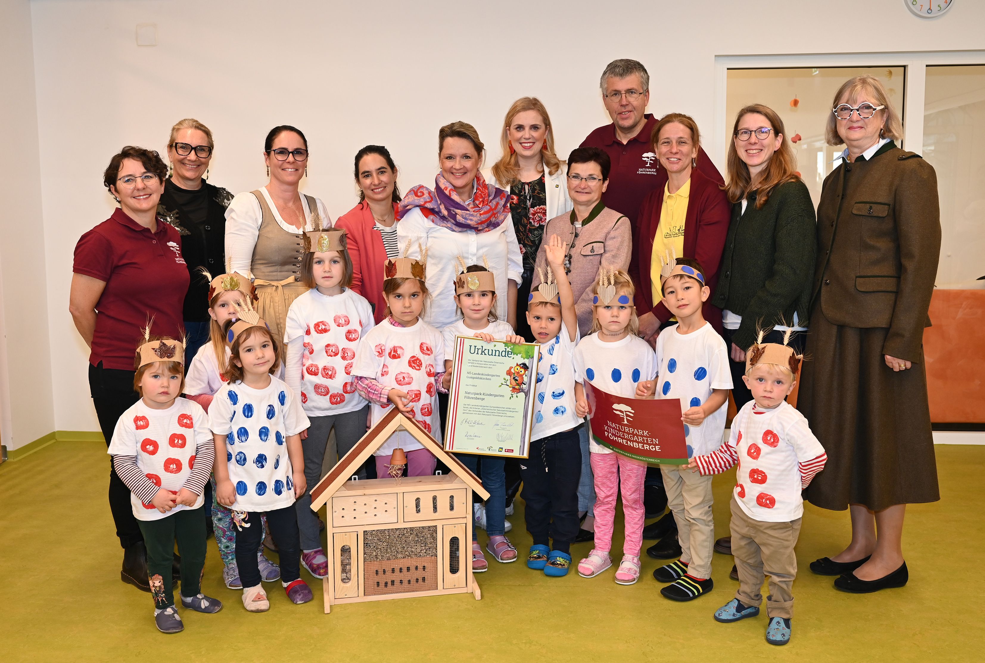 Ehrengäste, Kindergartenleitung und Kinder posieren mit der Naturpark-Kindergarten Urkunde für ein Gruppenfoto.