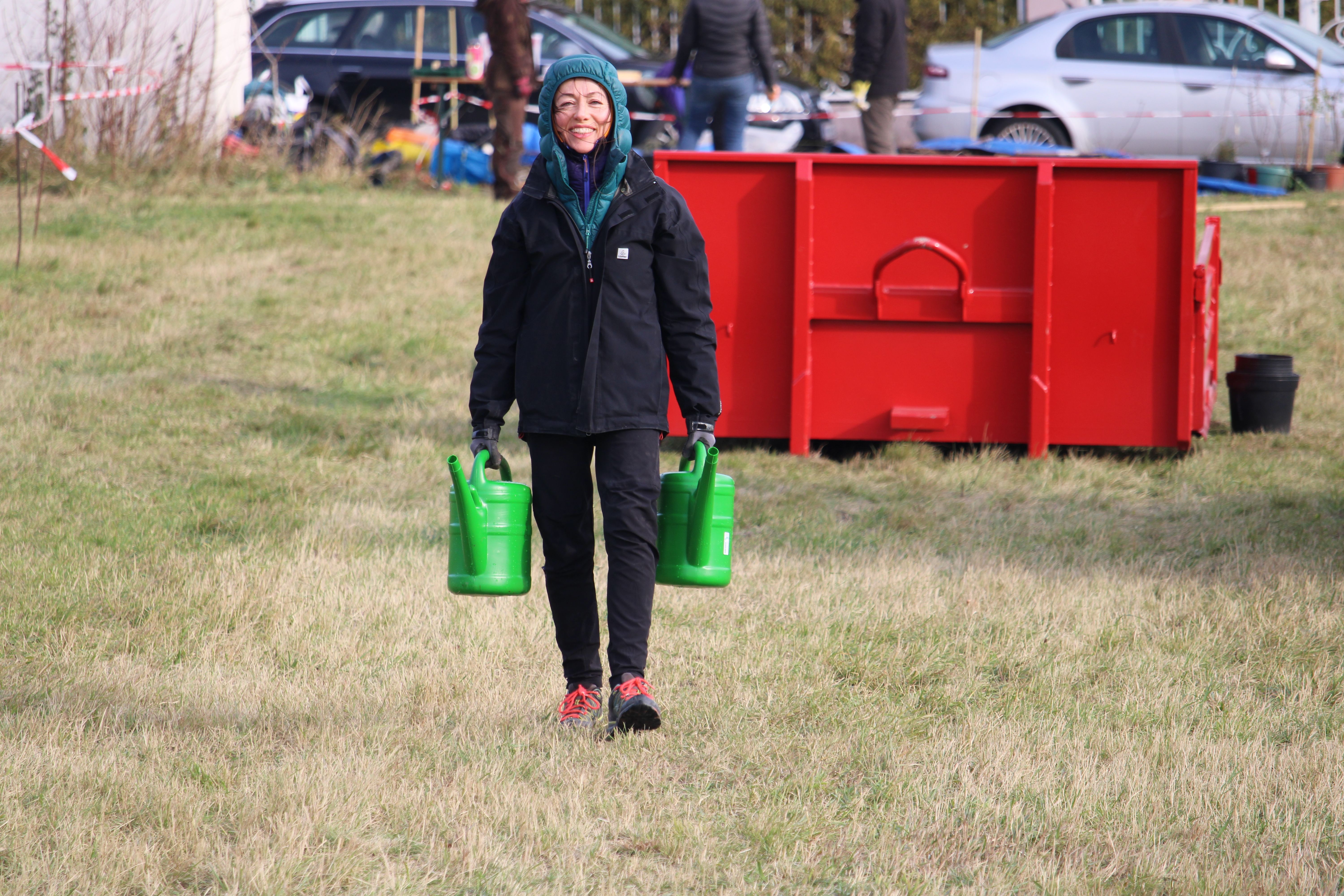 Praktikantin schleppt Gießkannen zu den Pflanzlöchern.