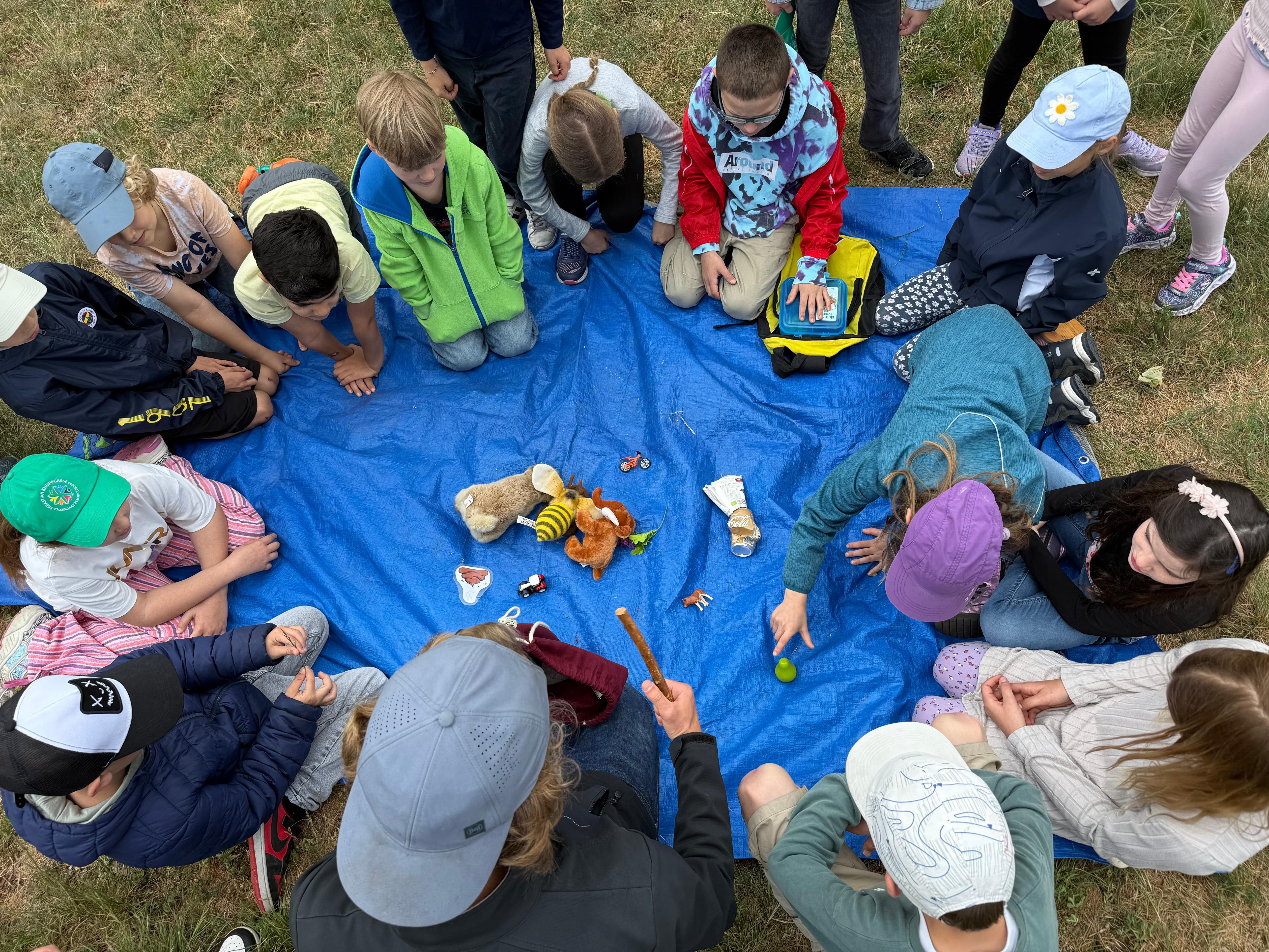 Kinder im Sitzkreis um Wiesen-Gegenstände