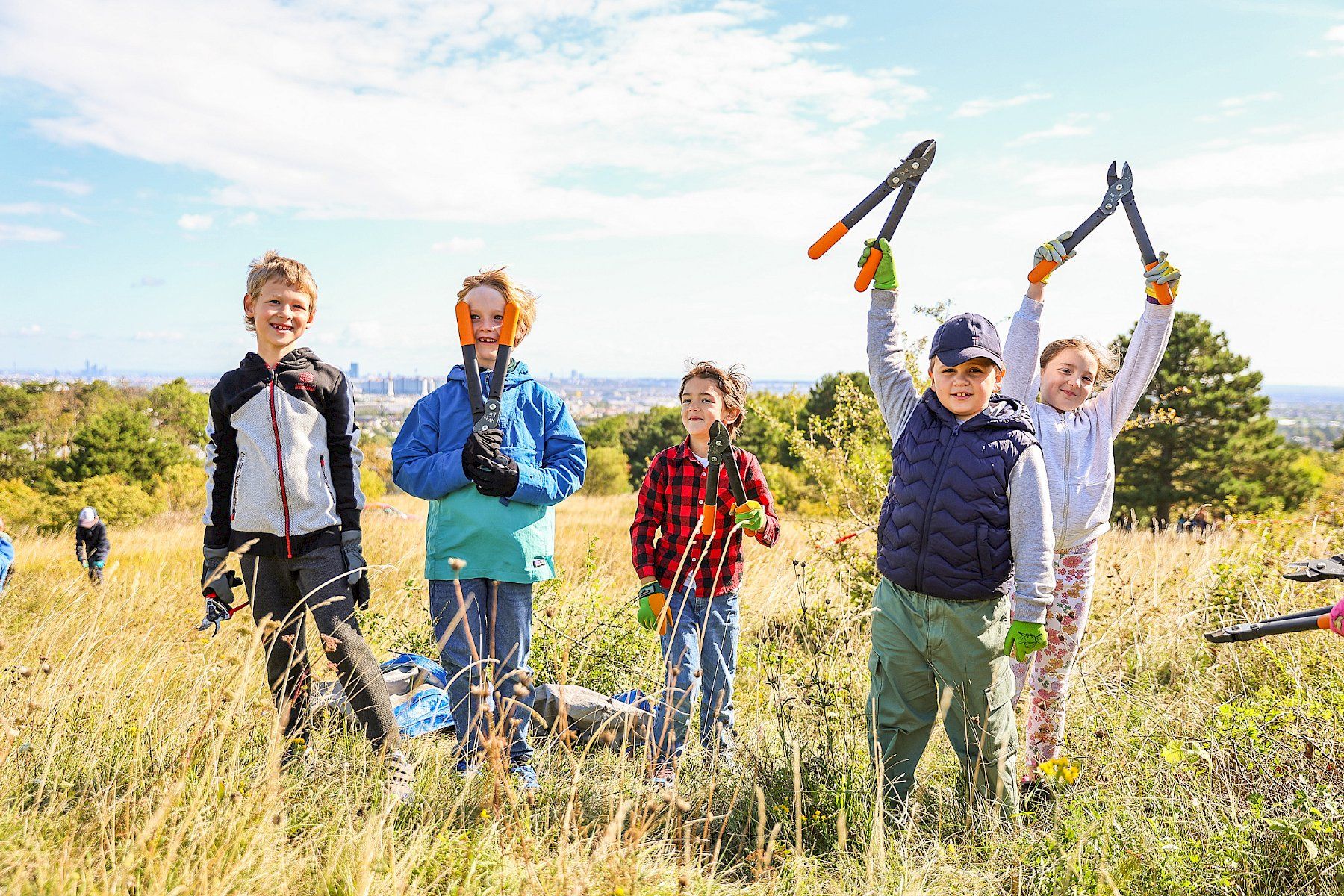 Strahlende Kinder halten auf der Perchtoldsdorfer Heide ihre Scheren nach einem erfolgreichen Pflegeeinsatz in die Höhe.