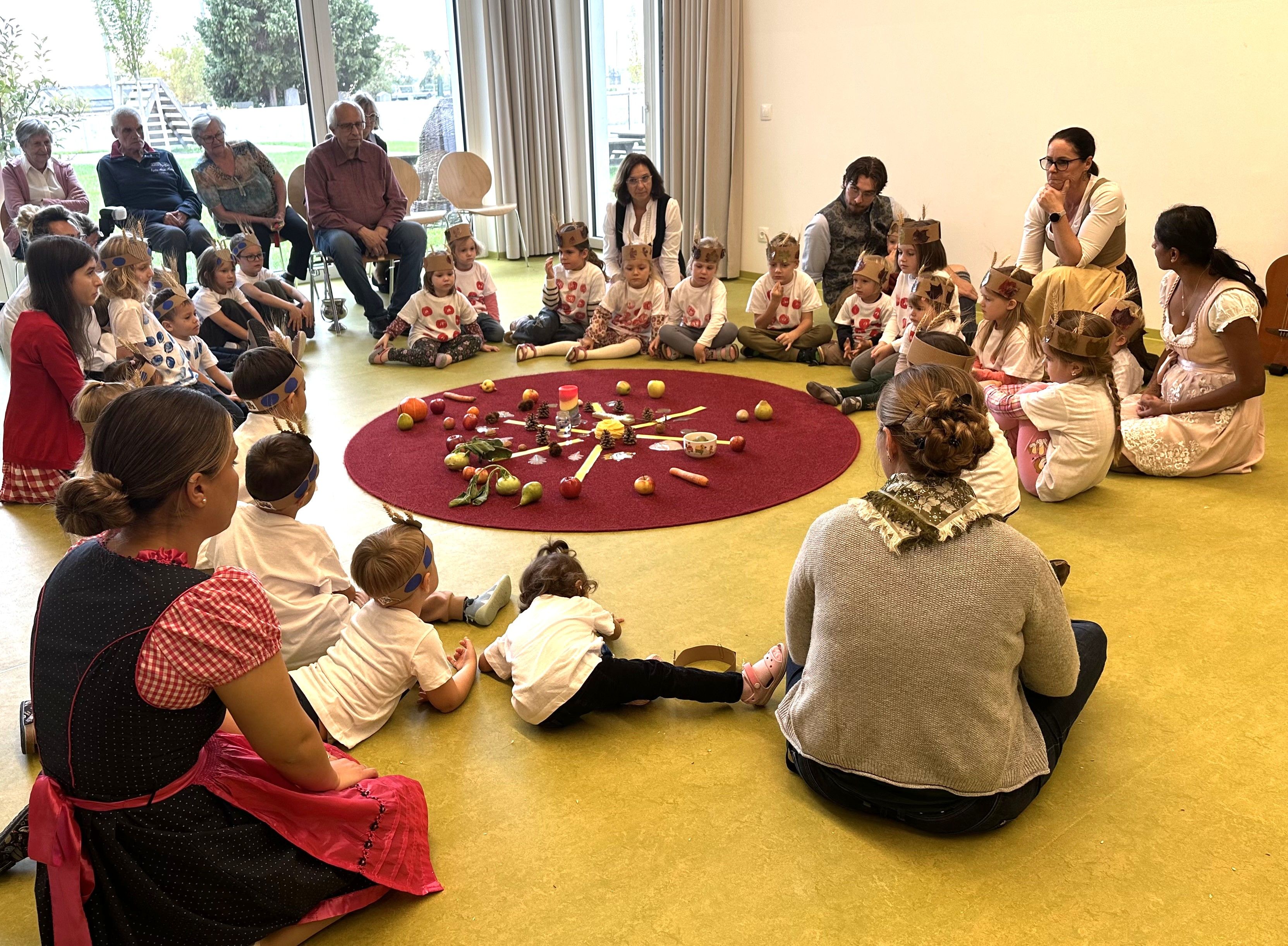 Kinder, Pädagoginnen und Ehrengäste sitzen im Kreis feiern Erntedank.